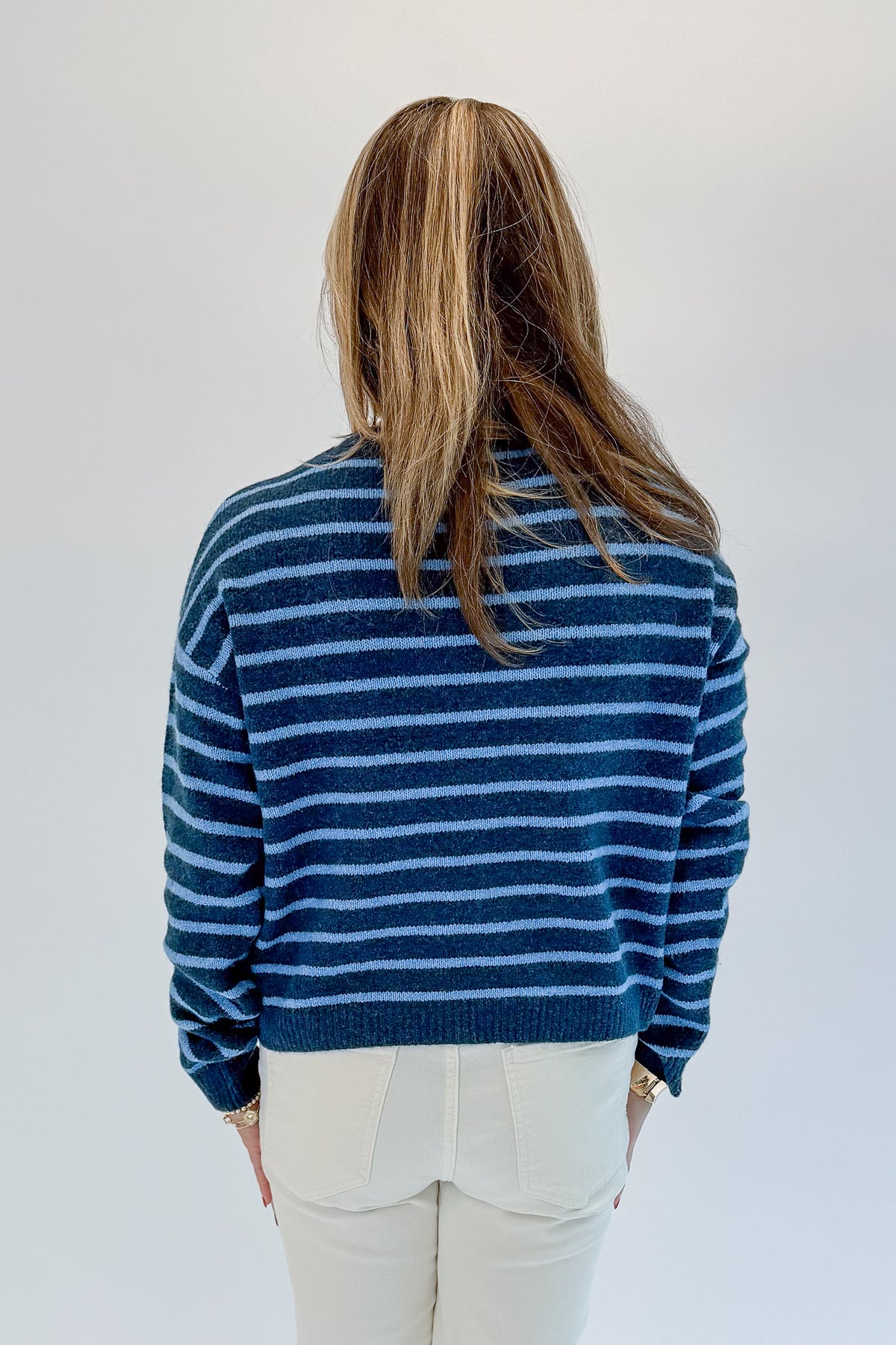 Back view of woman wearing Swagger Boutique’s Blue Striped Sweater with jeans against white studio background.