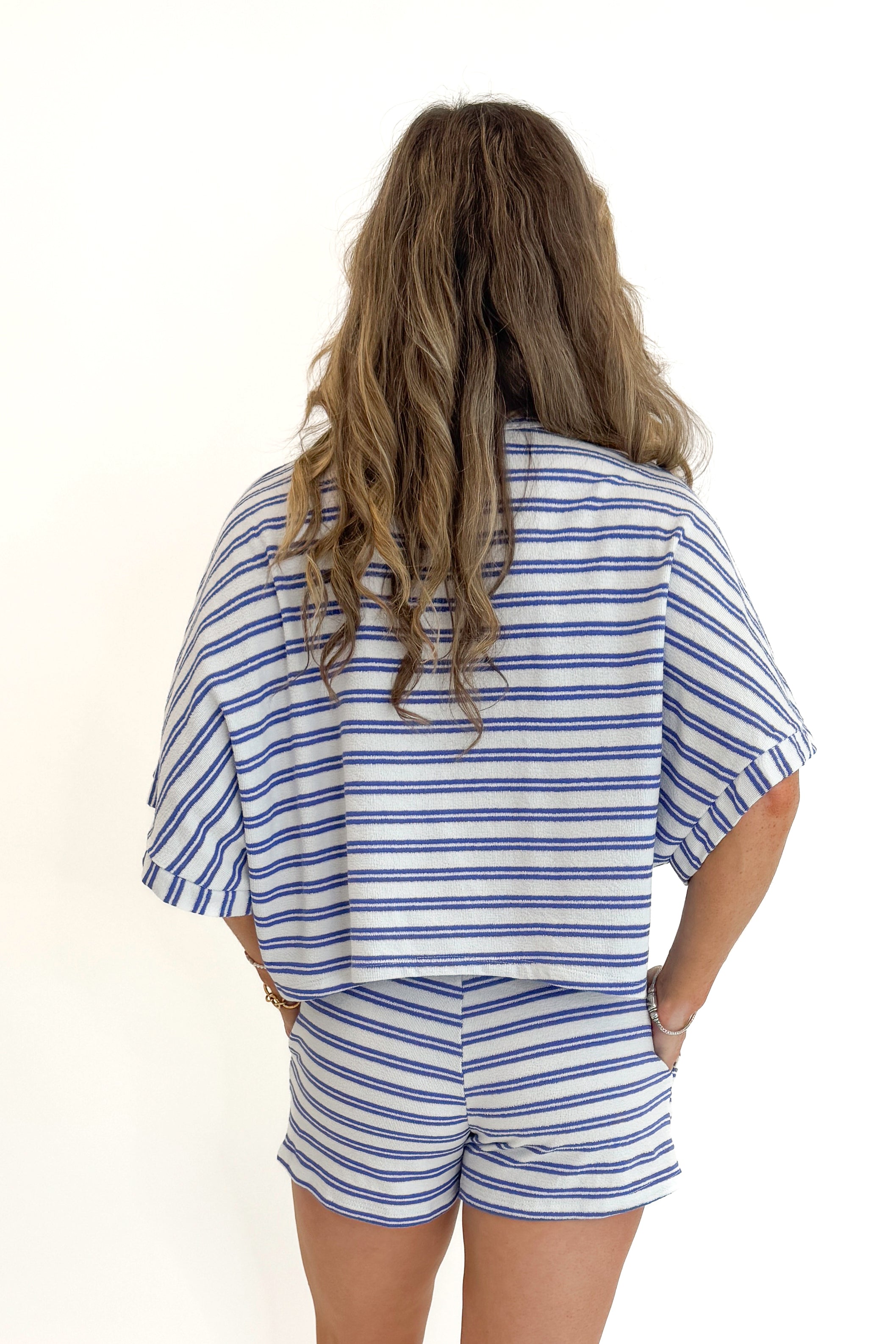 Back view of woman wearing Swagger Boutique’s Blue Striped Terry Cloth Shorts with matching Blue Striped Terry Cloth Top against white studio background.