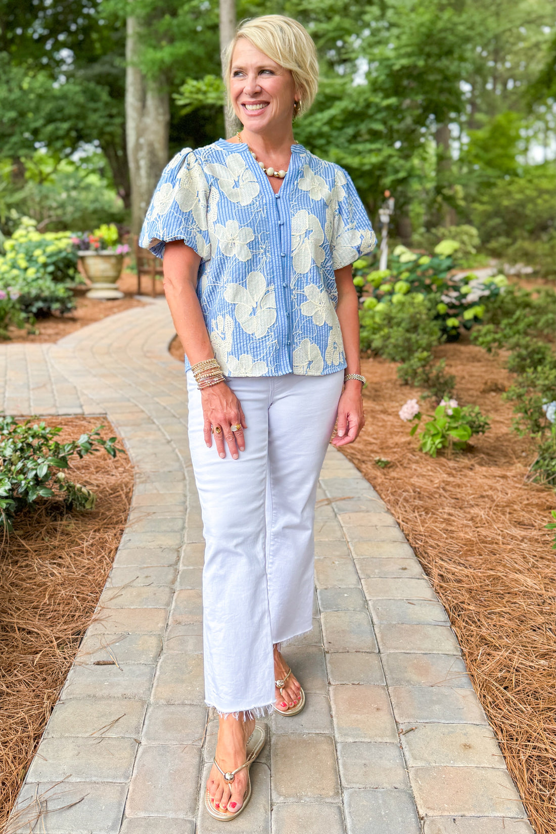 Woman wearing a blue floral blouse and white jeans walking down a path.