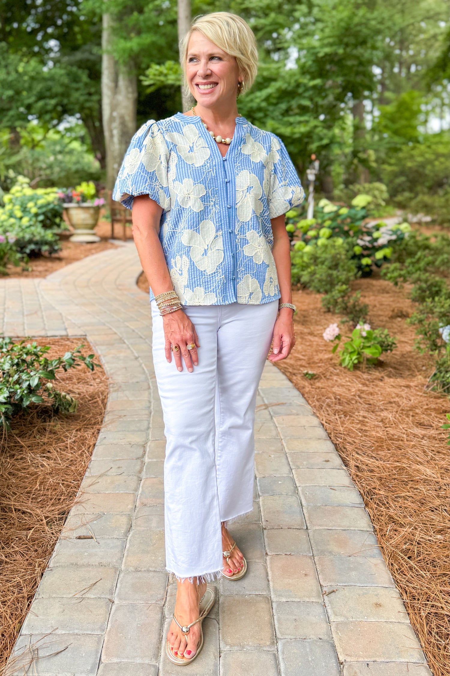 Woman wearing a blue floral blouse and white jeans walking down a path.
