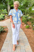 Woman wearing a blue floral blouse and white jeans walking down a path.