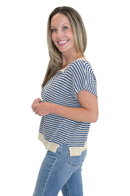 Side view of woman wearing Swagger Boutique’s Blue &amp; Beige Striped Sleeveless Sweater with jeans against white studio background.