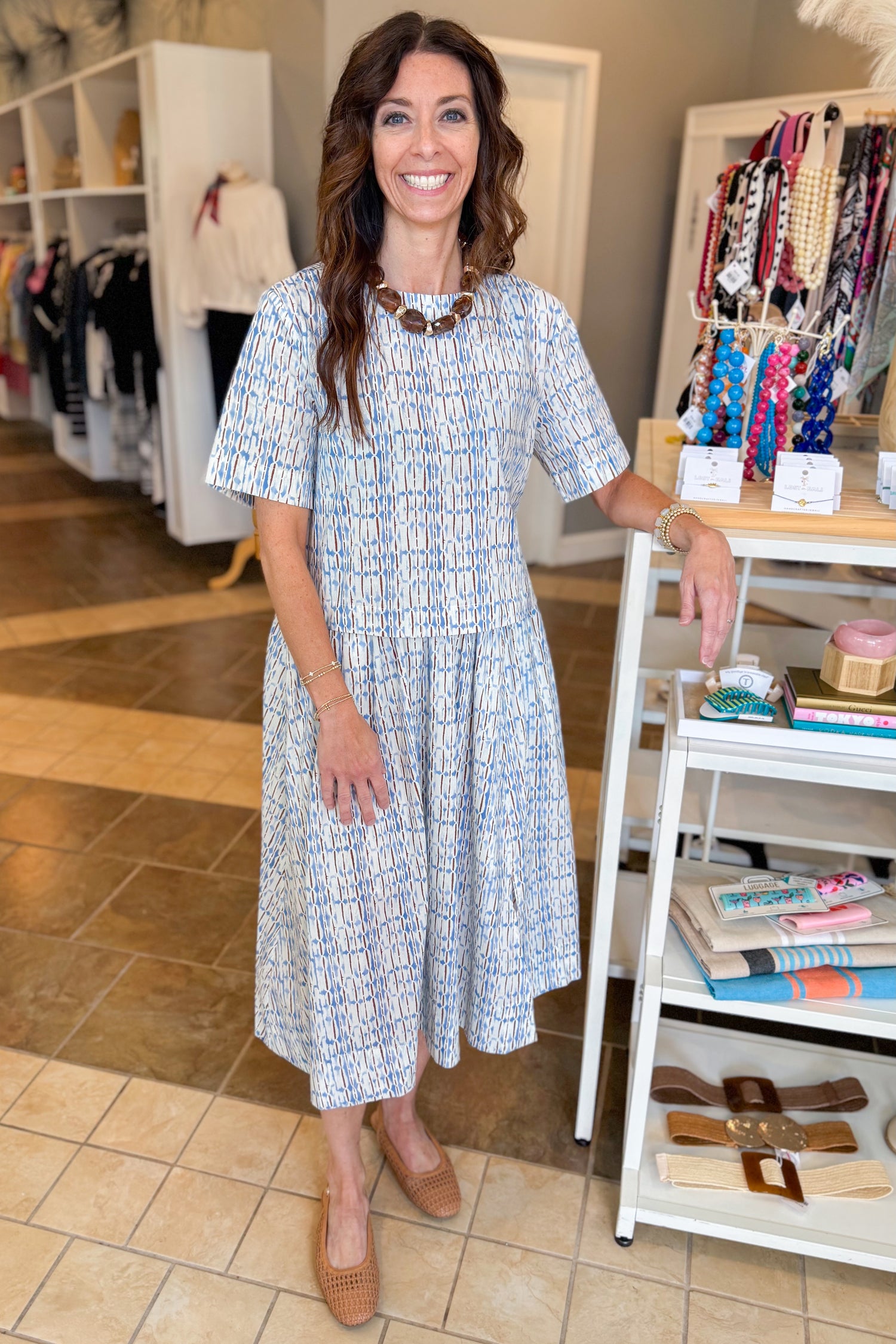 Front view of woman wearing Swagger Boutique’s Blue &amp; Brown Abstract Print Short Sleeve Top with matching skirt standing at the store.
