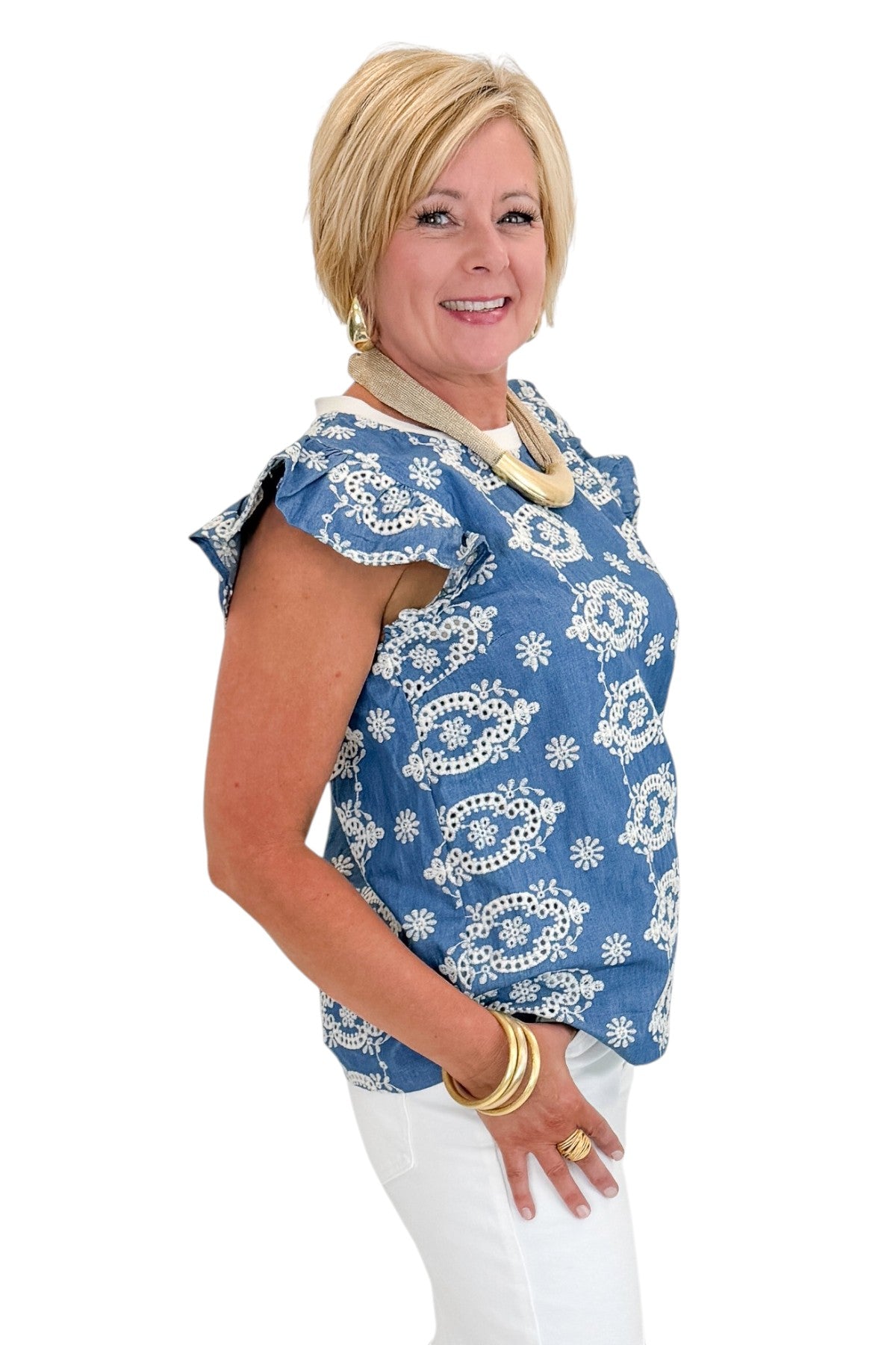 Side view of woman wearing Swagger Boutique’s Blue &amp; Cream Embroidered Top with jeans against white studio background.