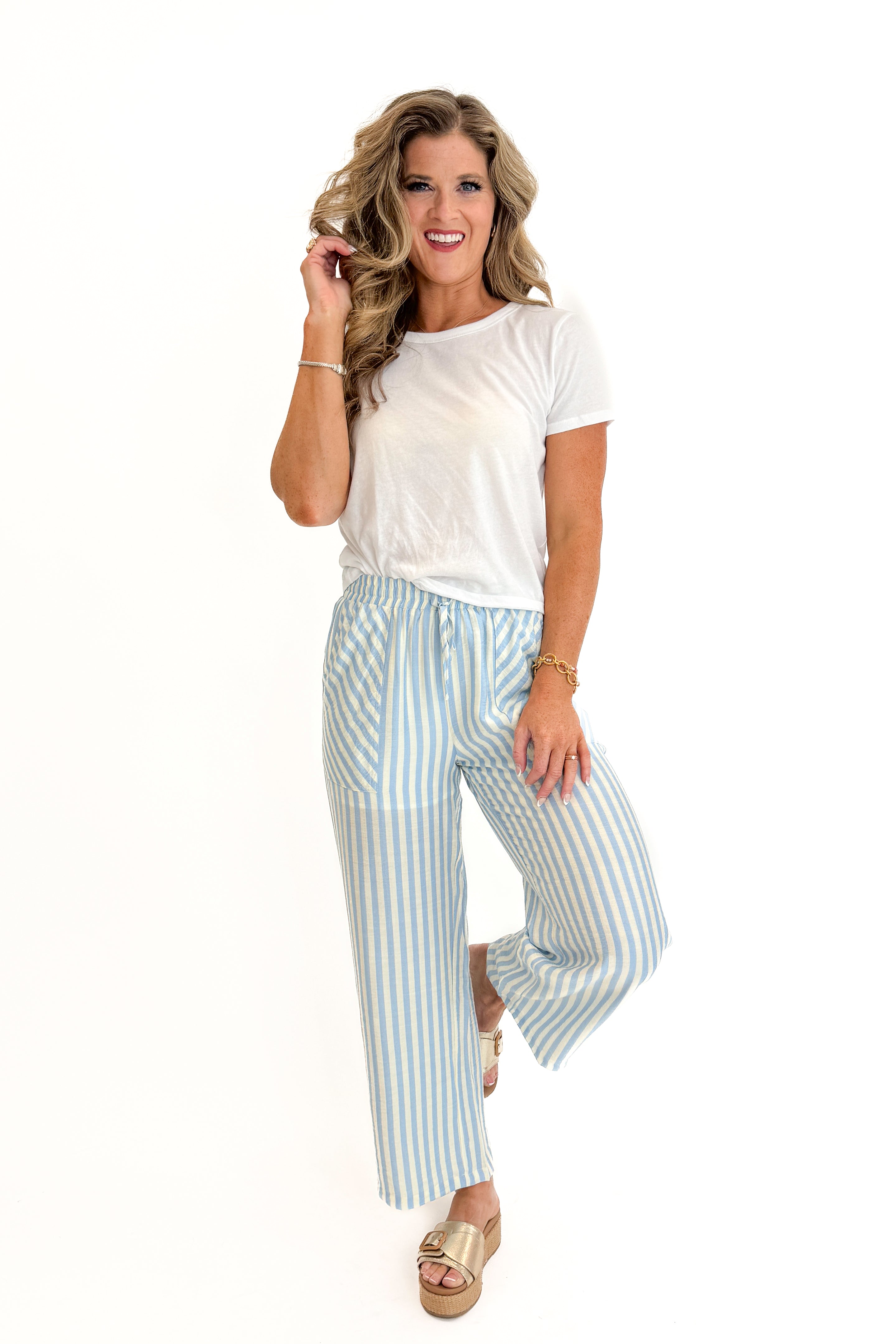 Front view of woman wearing Swagger Boutique’s Blue &amp; Cream Striped Pants with white top against white studio background.