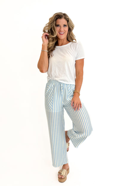 Front view of woman wearing Swagger Boutique’s Blue &amp; Cream Striped Pants with white top against white studio background.