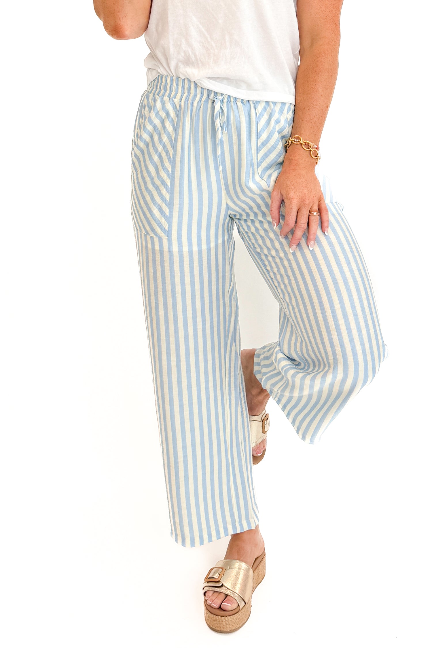 Front detail view of woman wearing Swagger Boutique’s Blue &amp; Cream Striped Pants with white top against white studio background.