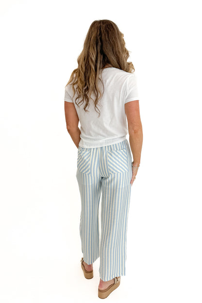 Back view of woman wearing Swagger Boutique’s Blue &amp; Cream Striped Pants with white top against white studio background.