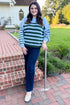 Front view of woman wearing Swagger Boutique’s Blue & Green Striped Sweater with jeans leaning against a railing outside.