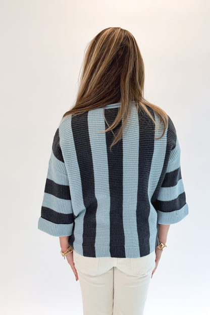 Back view of woman wearing Swagger Boutique’s Blue &amp; Grey Striped 3/4 Sleeve Sweater with jeans against white studio background.