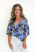 Front view of woman wearing Swagger Boutique’s Blue & Navy Tropical Printed 3/4 Sleeve Top with jeans against white studio background.