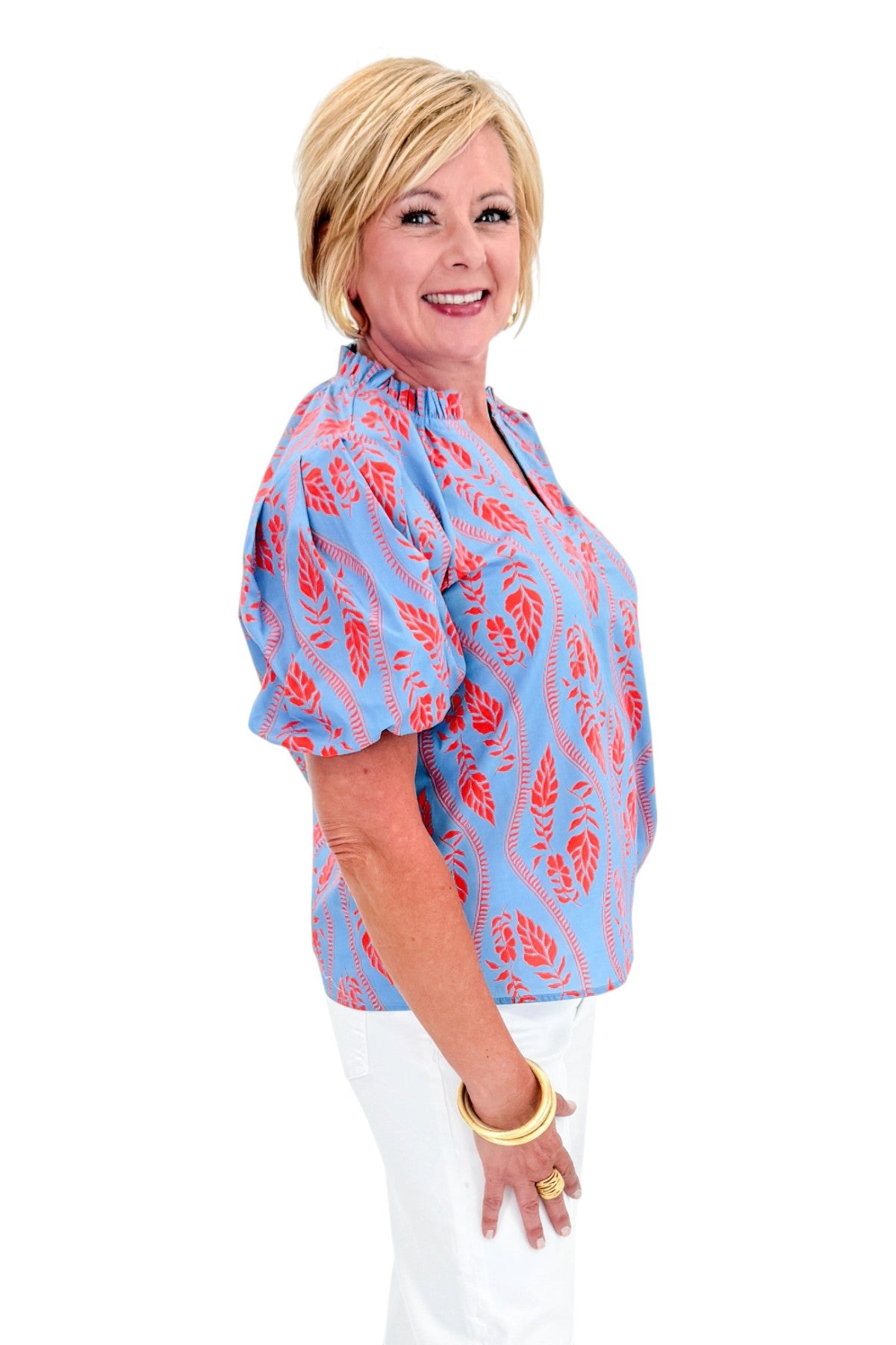Side view of woman wearing Swagger Boutique’s Blue &amp; Orange Botanical Print Short Sleeve Top with jeans against white studio background.