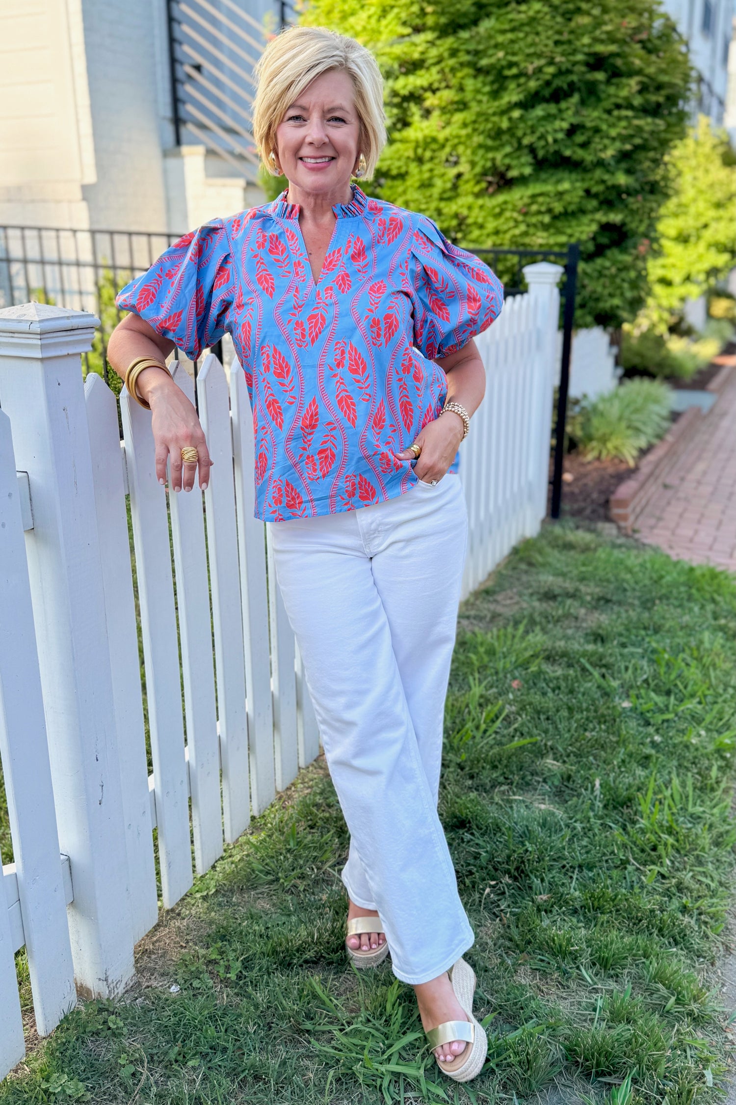 Front view of woman wearing Swagger Boutique’s Blue &amp; Orange Botanical Print Short Sleeve Top with jeans standing outside in a yard.