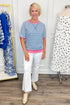 Front view of woman wearing Swagger Boutique’s Blue & Pink Striped Short Sleeve Sweatshirt with jeans with clothing hanging in the background.