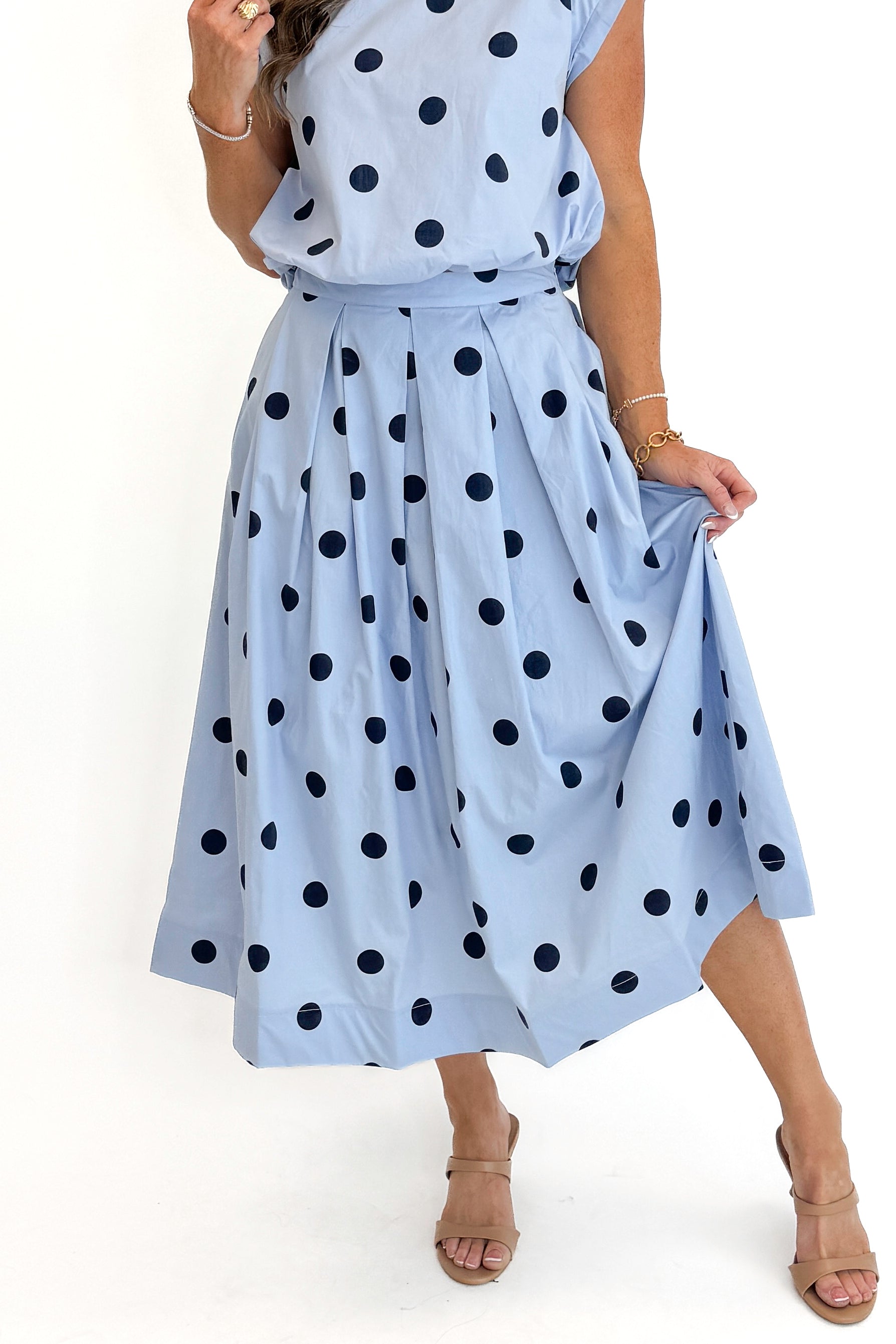 Front detail view of woman wearing Swagger Boutique’s Blue Polka Dot Bubble Hem Tank with matching Blue Polka Dot Pleated Midi Skirt against white studio background.