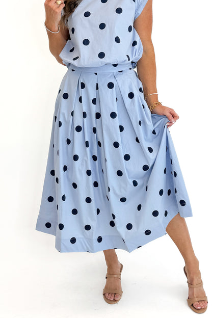 Front detail view of woman wearing Swagger Boutique’s Blue Polka Dot Bubble Hem Tank with matching Blue Polka Dot Pleated Midi Skirt against white studio background.