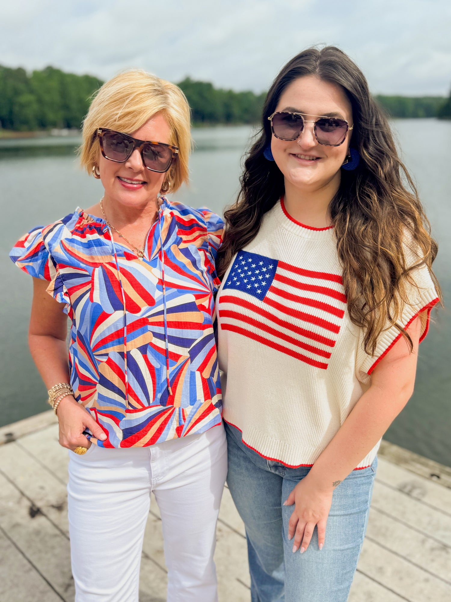 Front view of woman wearing Swagger Boutique’s Blue &amp; Red Printed Ruffle Sleeve Top by Skies Are Blue and woman wearing Flag sweater outside at the lake.