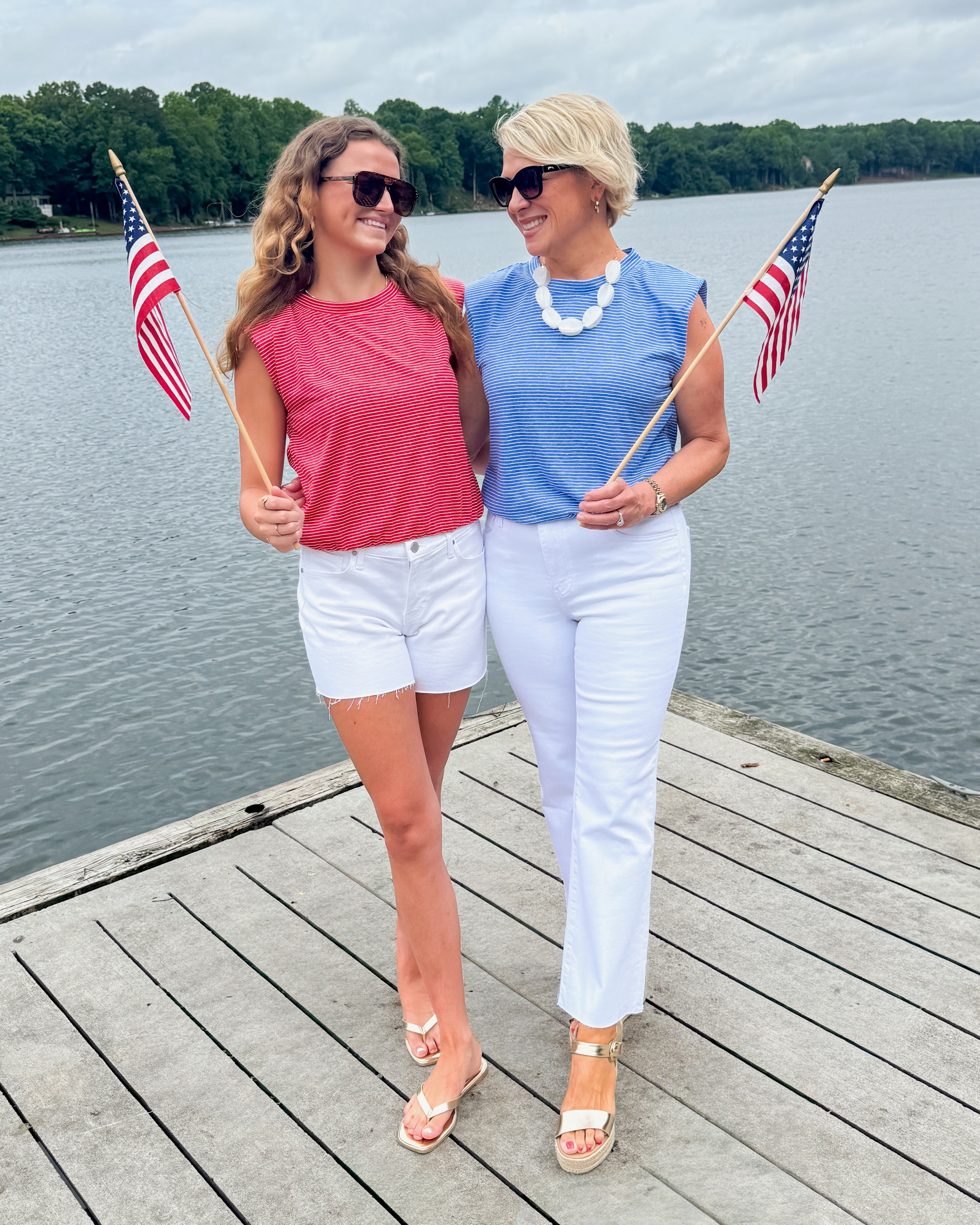 Front view of women wearing Swagger Boutique’s Red and Blue Striped Bubble Hem Sleeveless Tops standing outside at a dock at the lake.