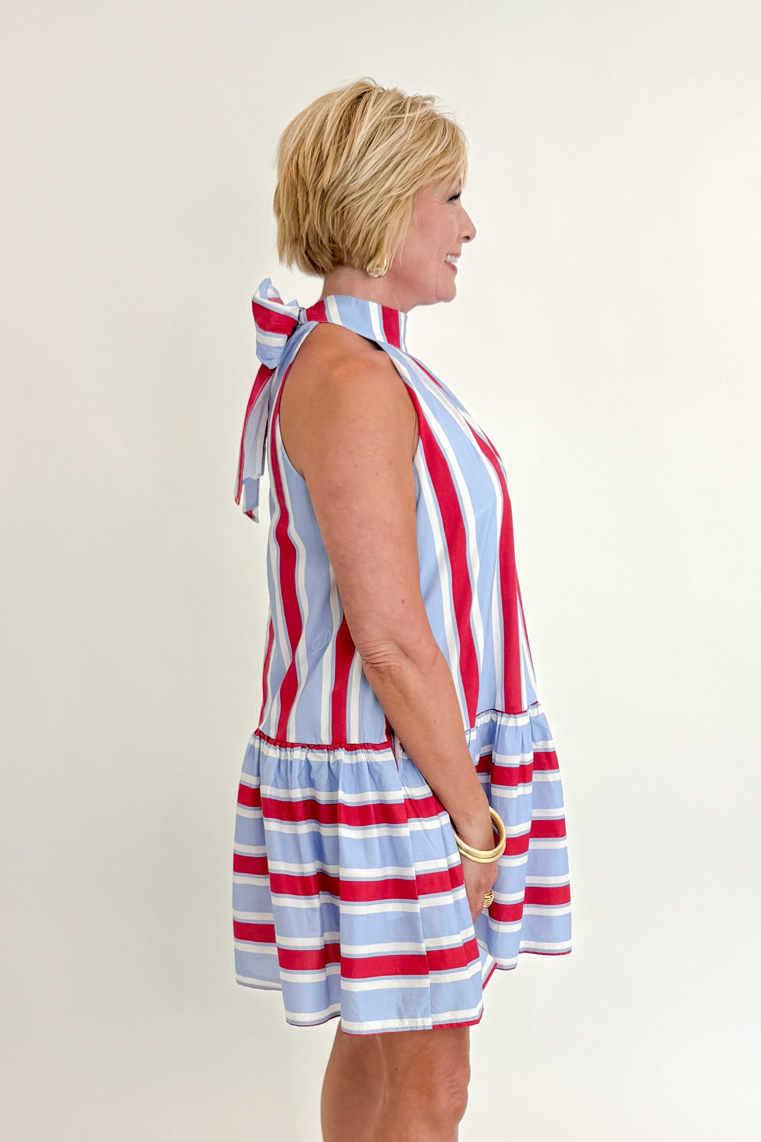 Side view of woman wearing Swagger Boutique’s Blue &amp; Red Striped Halter Neck Dress by Entro with sandals against white studio background.