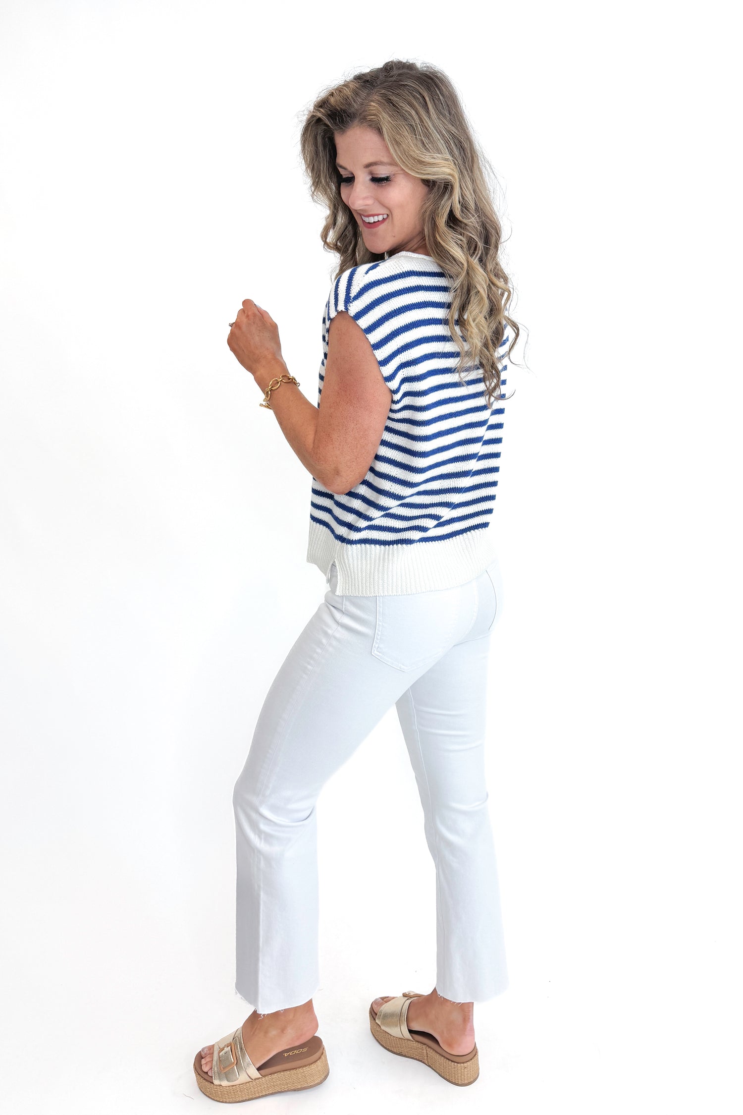 Side view of woman wearing Swagger Boutique’s Blue &amp; White Striped Sleeveless Sweater with jeans against white studio background.