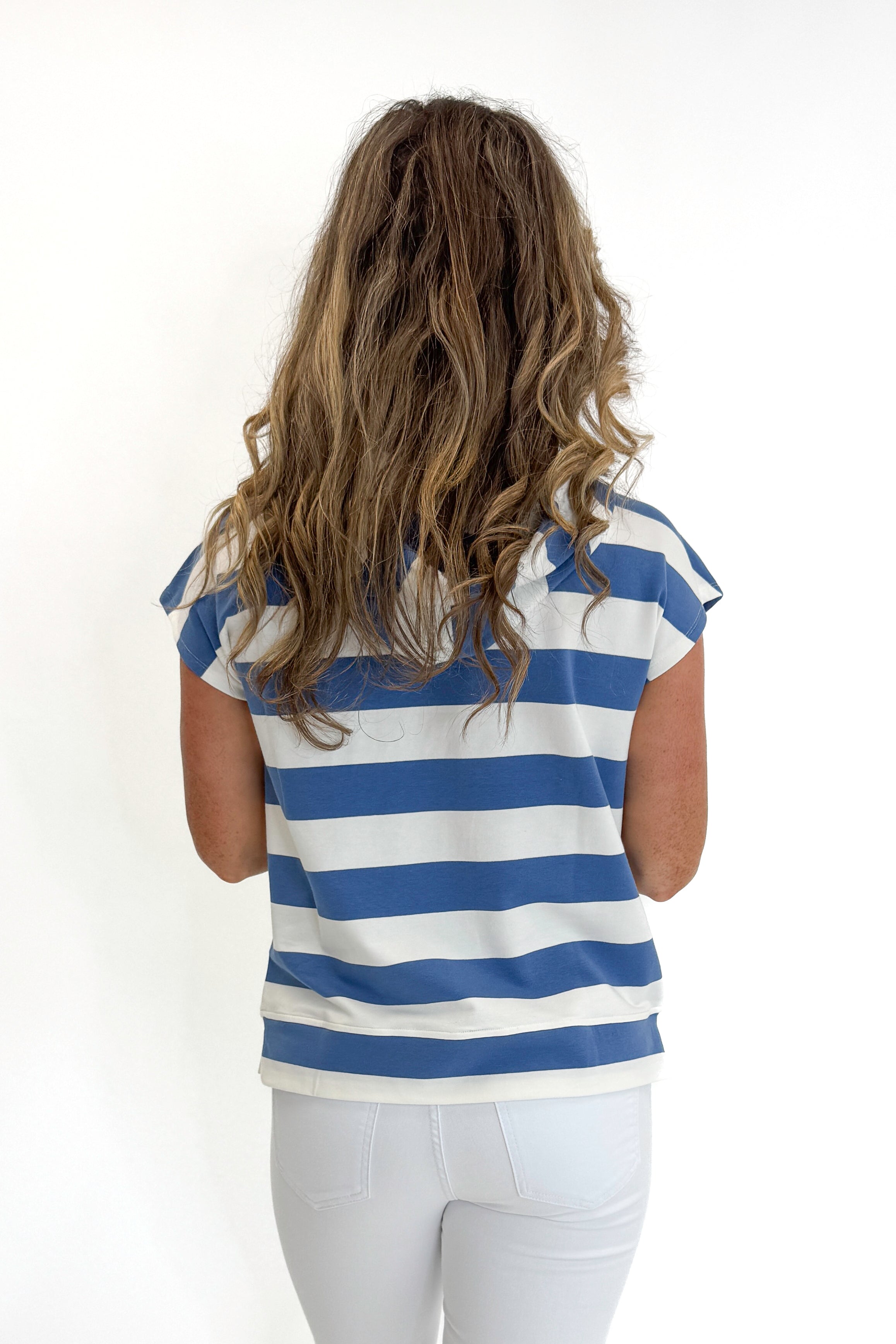 Back view of woman wearing Swagger Boutique’s Blue &amp; White Striped Sleeveless Sweatshirt with white jeans against white studio background.