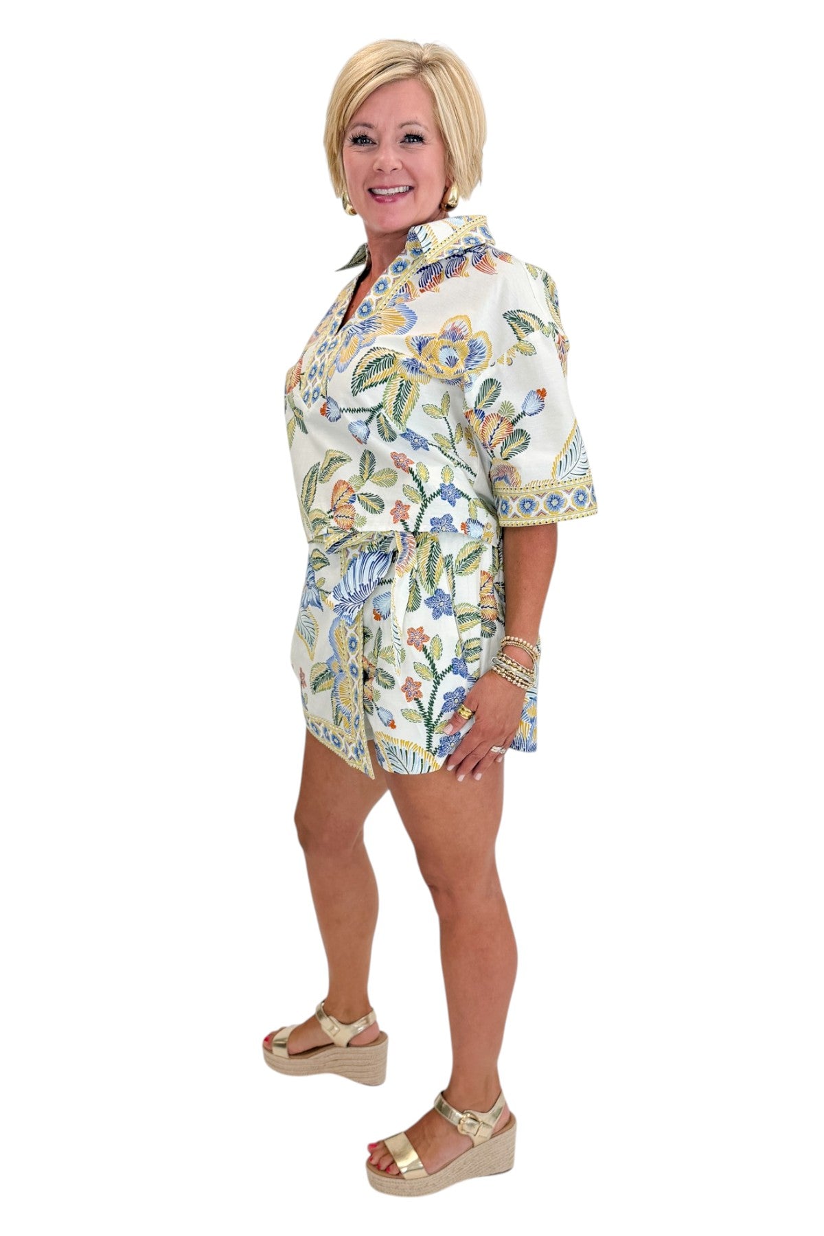 Side view of woman wearing Swagger Boutique’s Blue &amp; Yellow Floral Print Wrap Skort by Entro with matching top against white studio background.