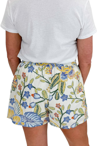 Back detail view of woman wearing Swagger Boutique’s Blue &amp; Yellow Floral Print Wrap Skort by Entro with white top against white studio background.