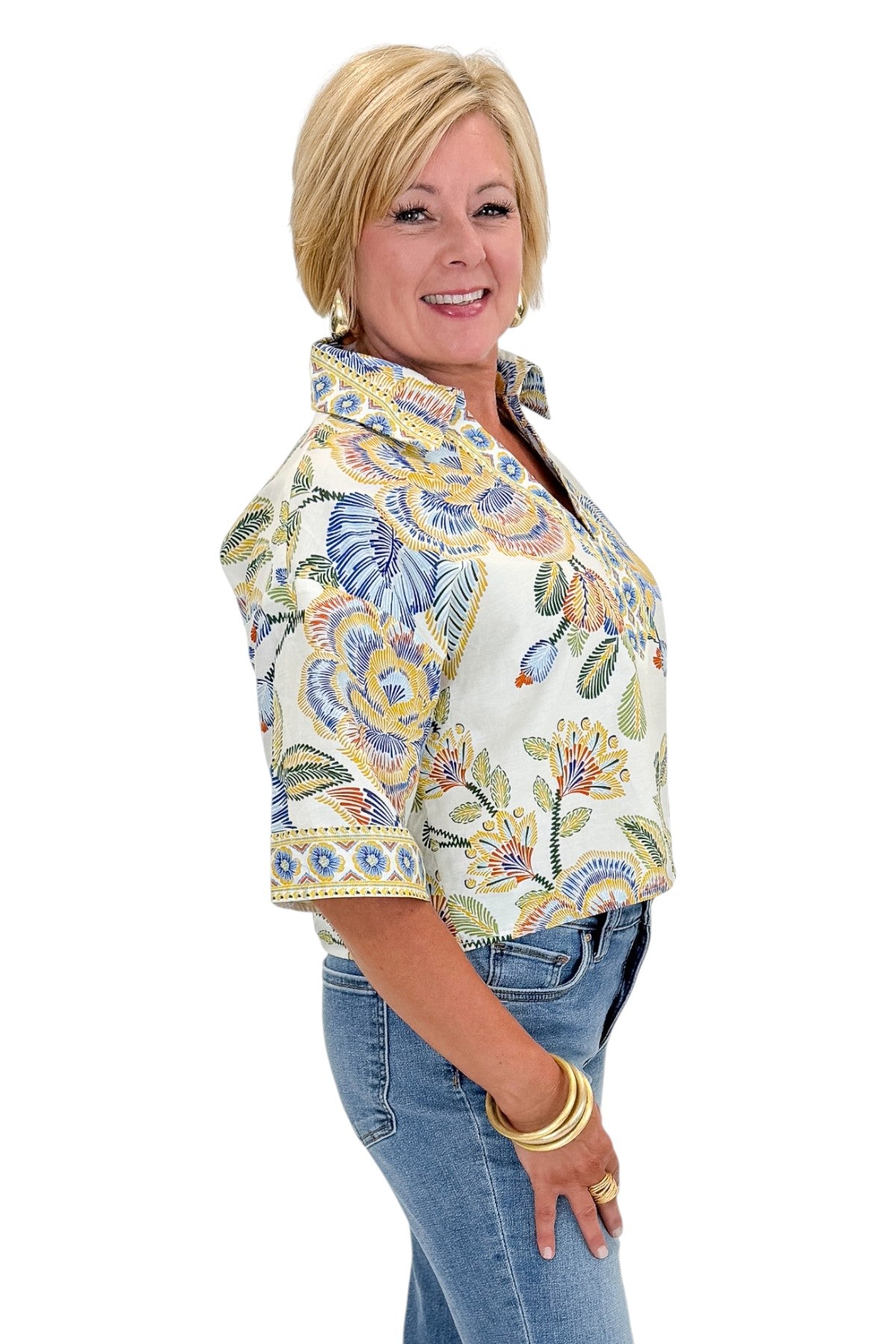Side view of woman wearing Swagger Boutique’s Blue &amp; Yellow Floral Print Collared Top with jeans against white studio background.
