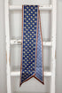 A blue patterned silk scarf with gold and white circular motifs and a brown border, hanging from a rustic white wooden ladder.