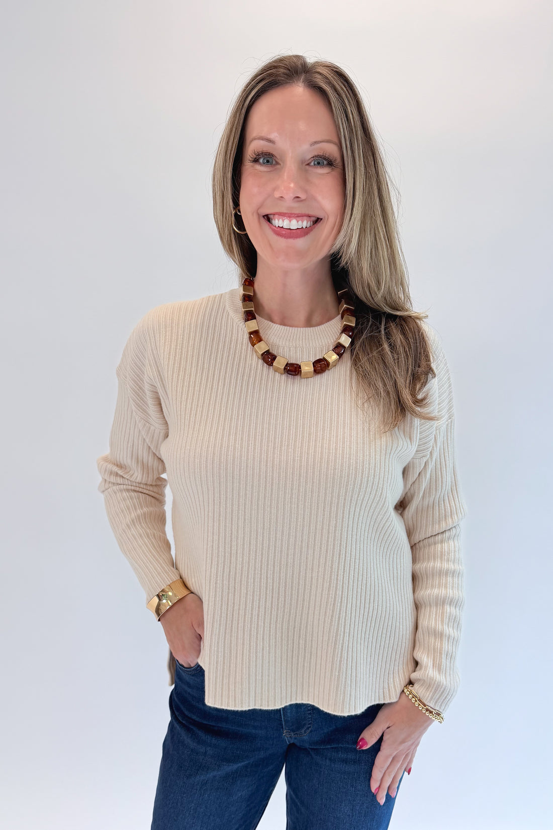 Front view of woman wearing Swagger Boutique’s Bone Ribbed Lightweight Sweater with jeans against white studio background.