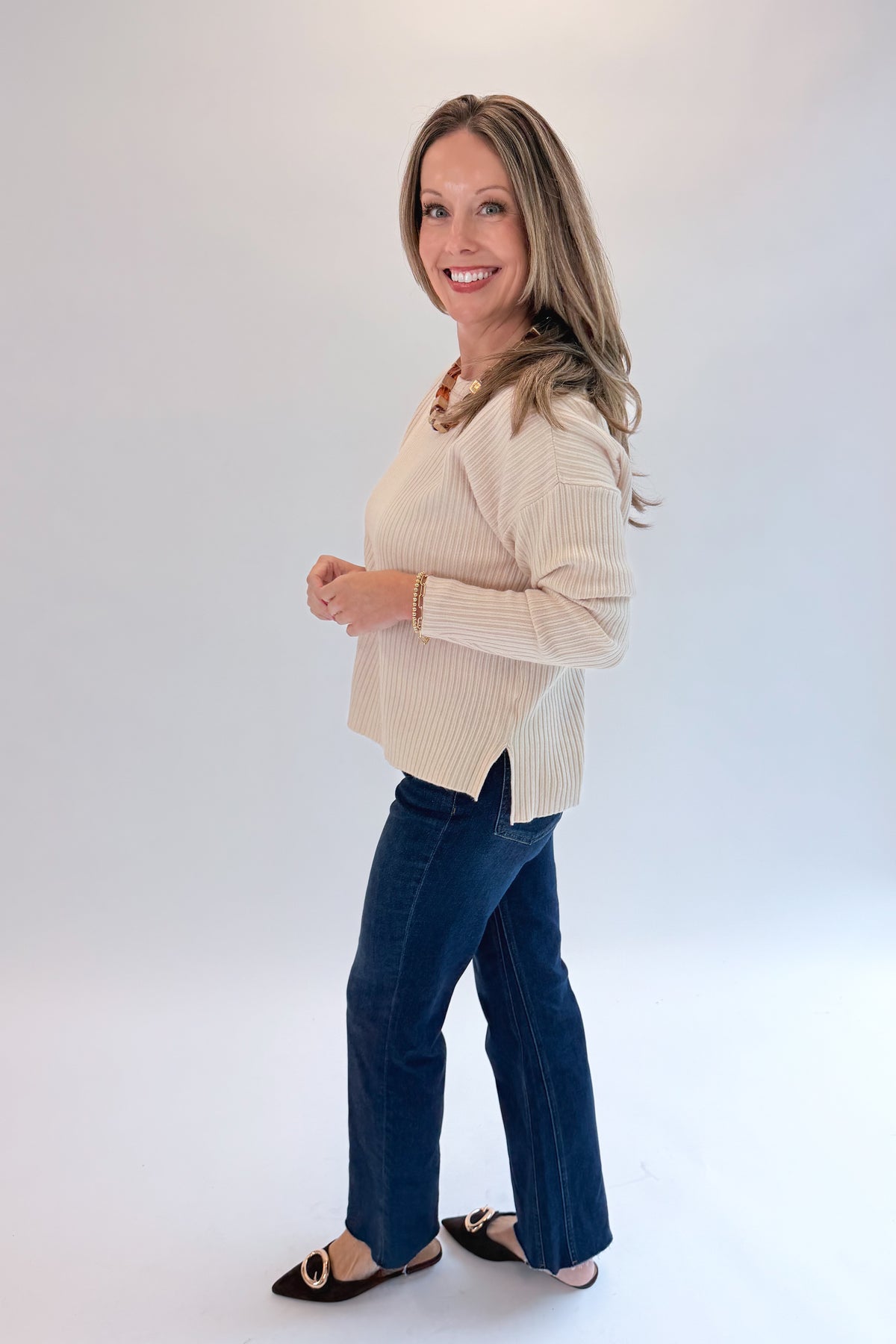 Side view of woman wearing Swagger Boutique’s Bone Ribbed Lightweight Sweater with jeans against white studio background.