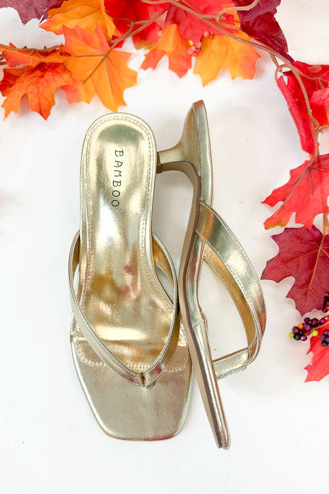 Brat- Gold Thong Kitten Heels against white studio background with leaves around.