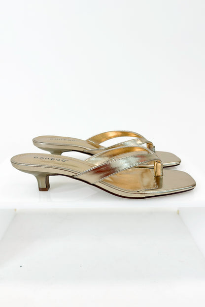 Brat- Gold Thong Kitten Heels against white studio background side view.