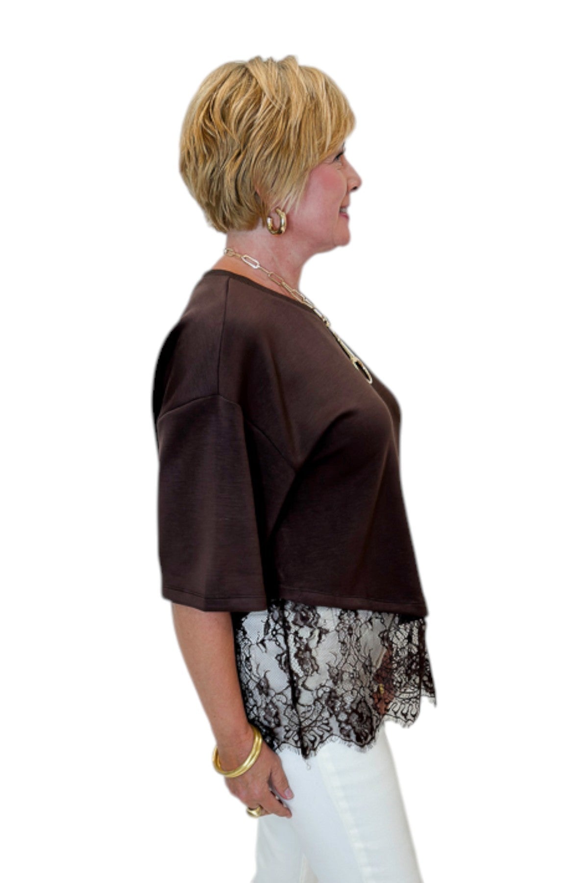 Side view of woman wearing Swagger Boutique’s Brown Asymmetrical Lace Hem Top by Entro with jeans against white studio background.