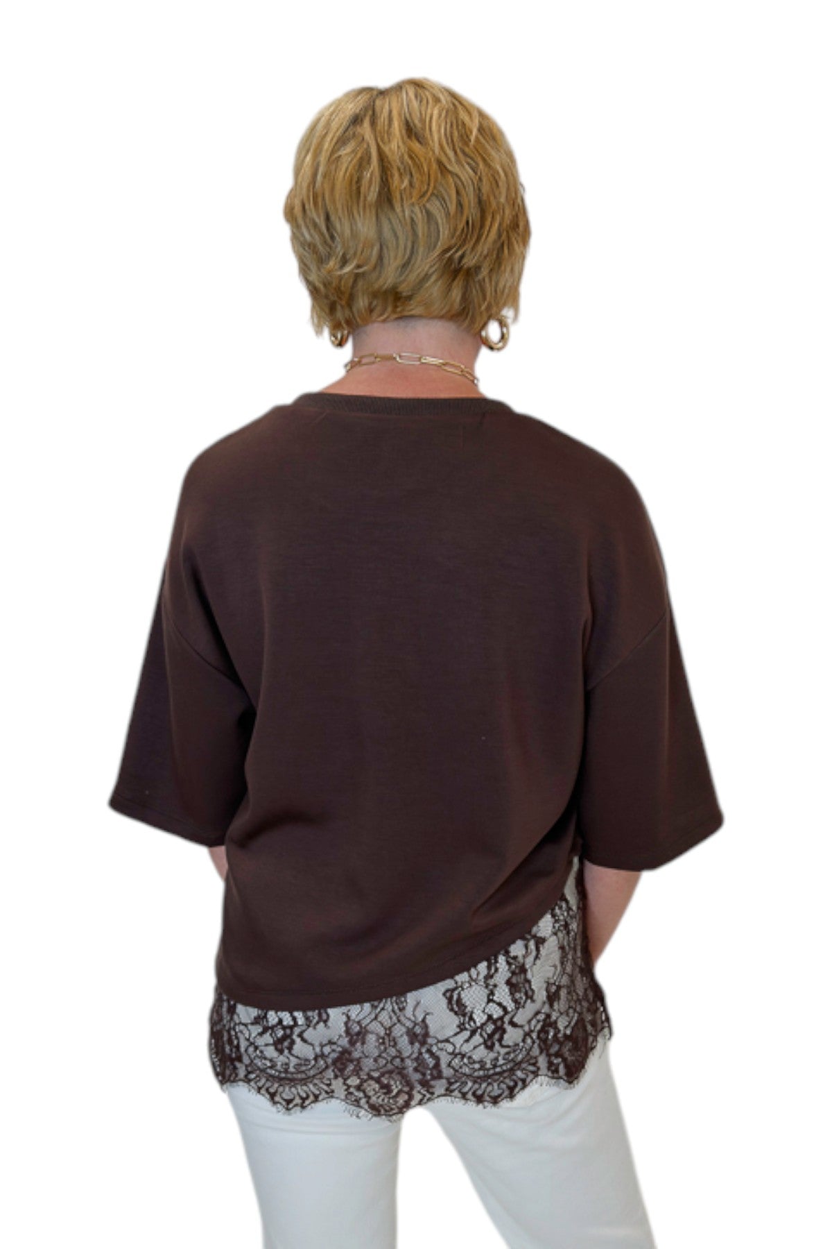 Back view of woman wearing Swagger Boutique’s Brown Asymmetrical Lace Hem Top by Entro with jeans against white studio background.