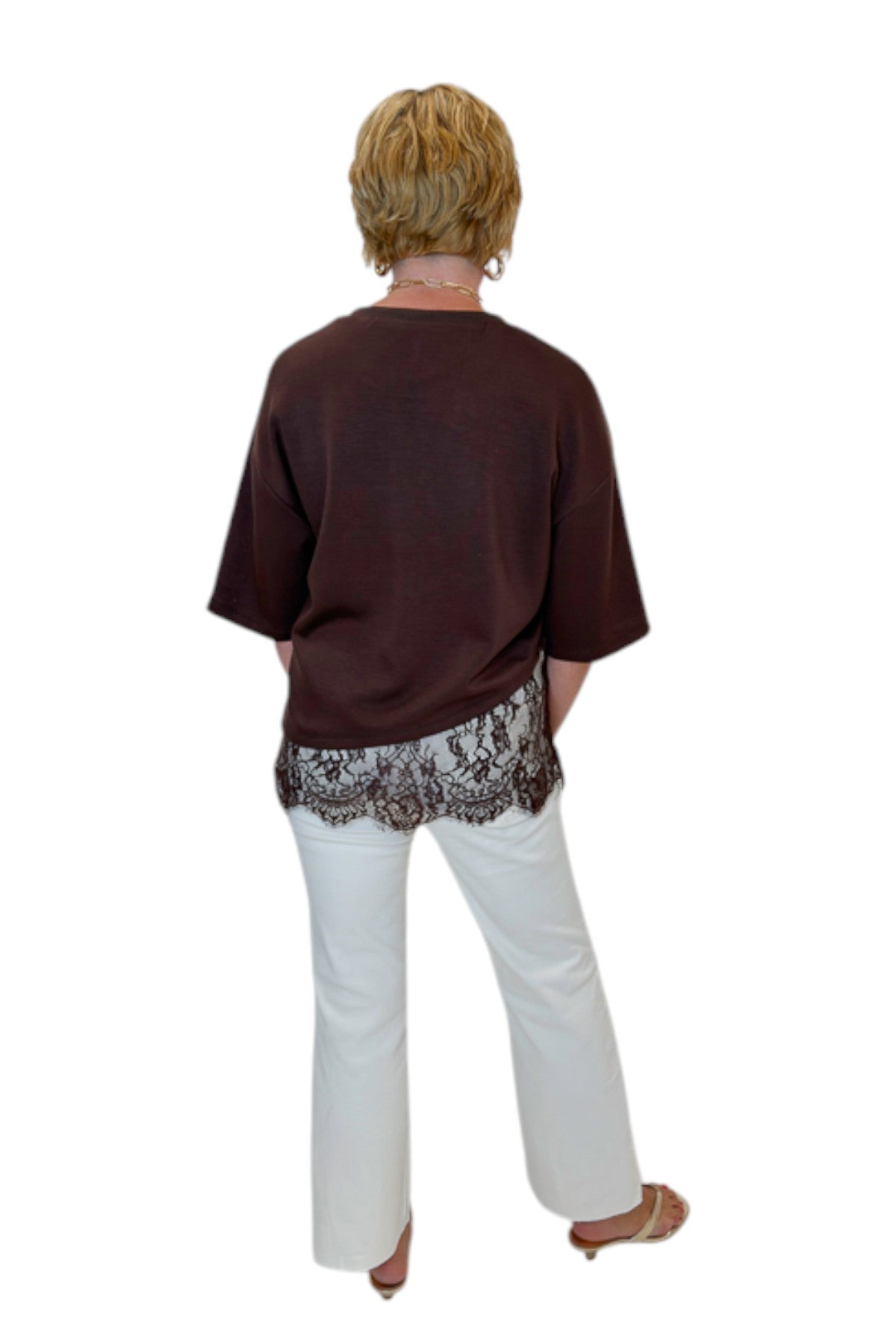 Back view of woman wearing Swagger Boutique’s Brown Asymmetrical Lace Hem Top by Entro with jeans against white studio background.
