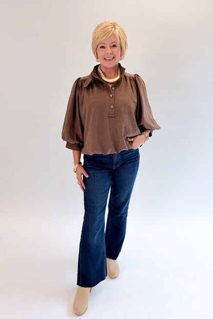 Front view of woman wearing Swagger Boutique’s Brown Bubble Hem Top With Buttons by Entro with jeans against white studio background.