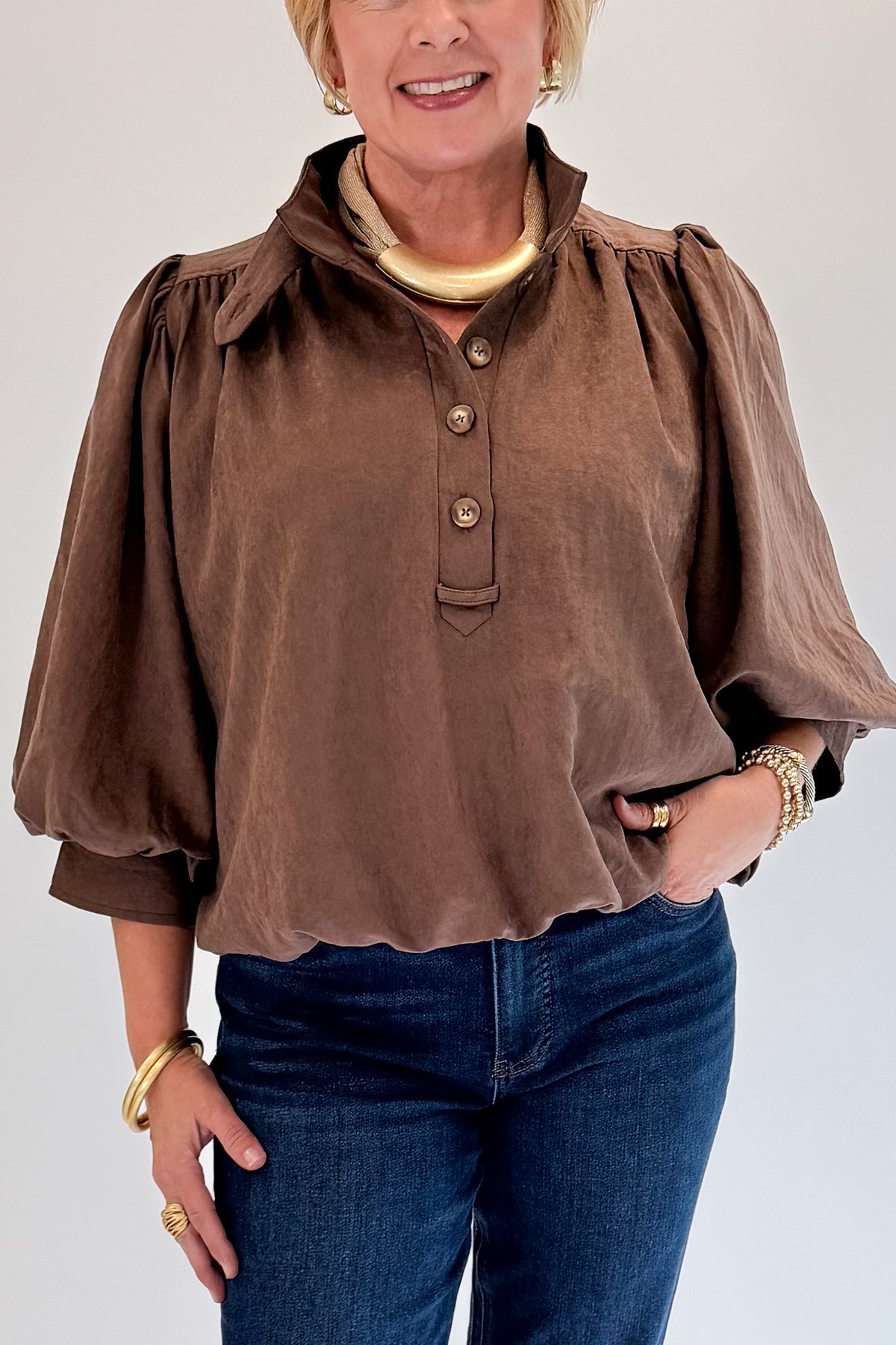 Front detail view of woman wearing Swagger Boutique’s Brown Bubble Hem Top With Buttons by Entro with jeans against white studio background.