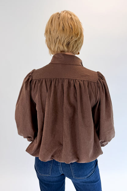 Back view of woman wearing Swagger Boutique’s Brown Bubble Hem Top With Buttons by Entro with jeans against white studio background.