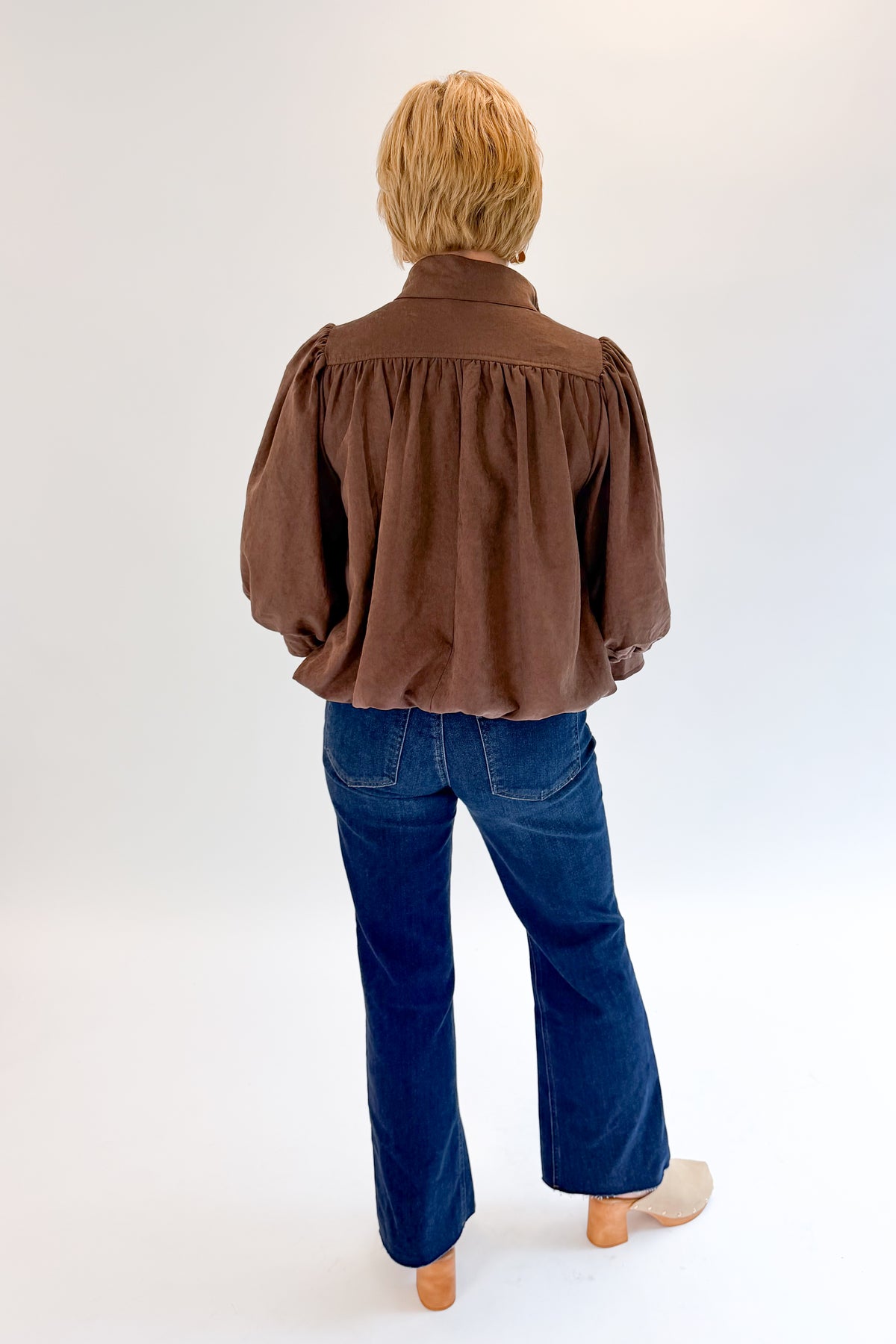 Back view of woman wearing Swagger Boutique’s Brown Bubble Hem Top With Buttons by Entro with jeans against white studio background.