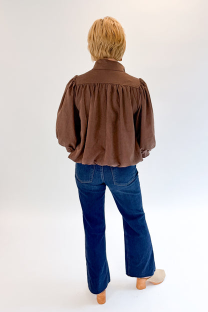 Back view of woman wearing Swagger Boutique’s Brown Bubble Hem Top With Buttons by Entro with jeans against white studio background.