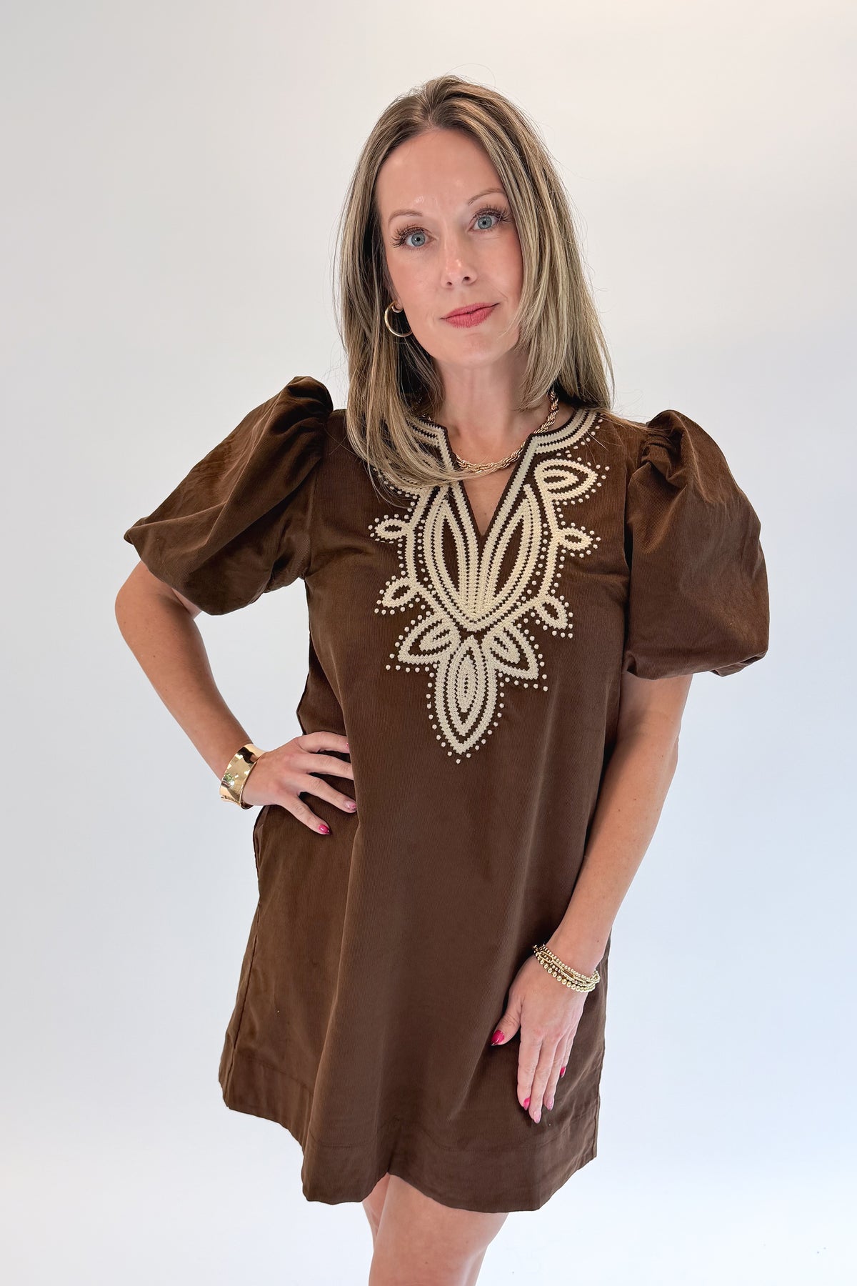 Front view of woman wearing Swagger Boutique’s Brown Embroidered Corduroy Dress with heels against white studio background.