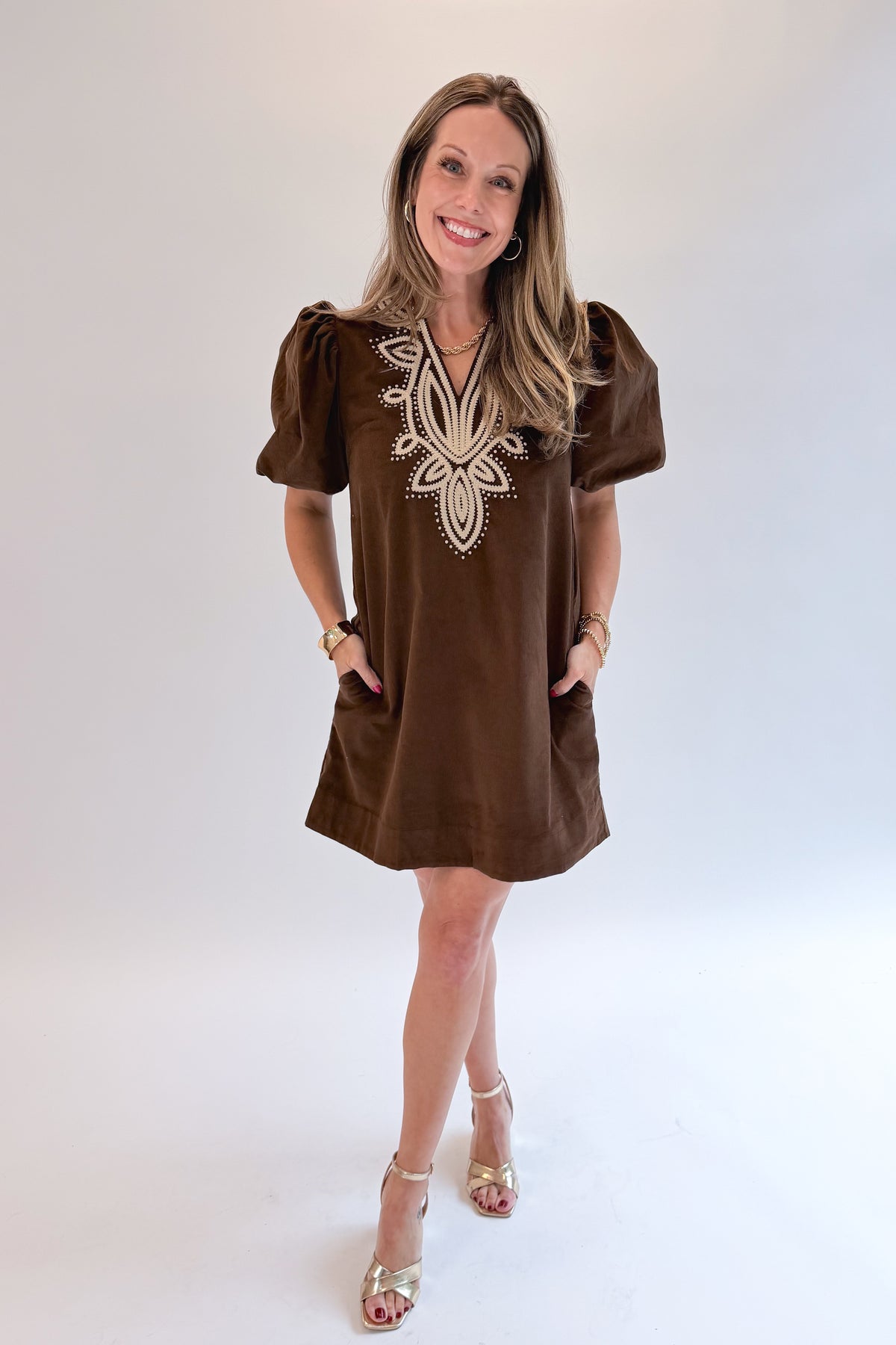 Front view of woman wearing Swagger Boutique’s Brown Embroidered Corduroy Dress with heels against white studio background.