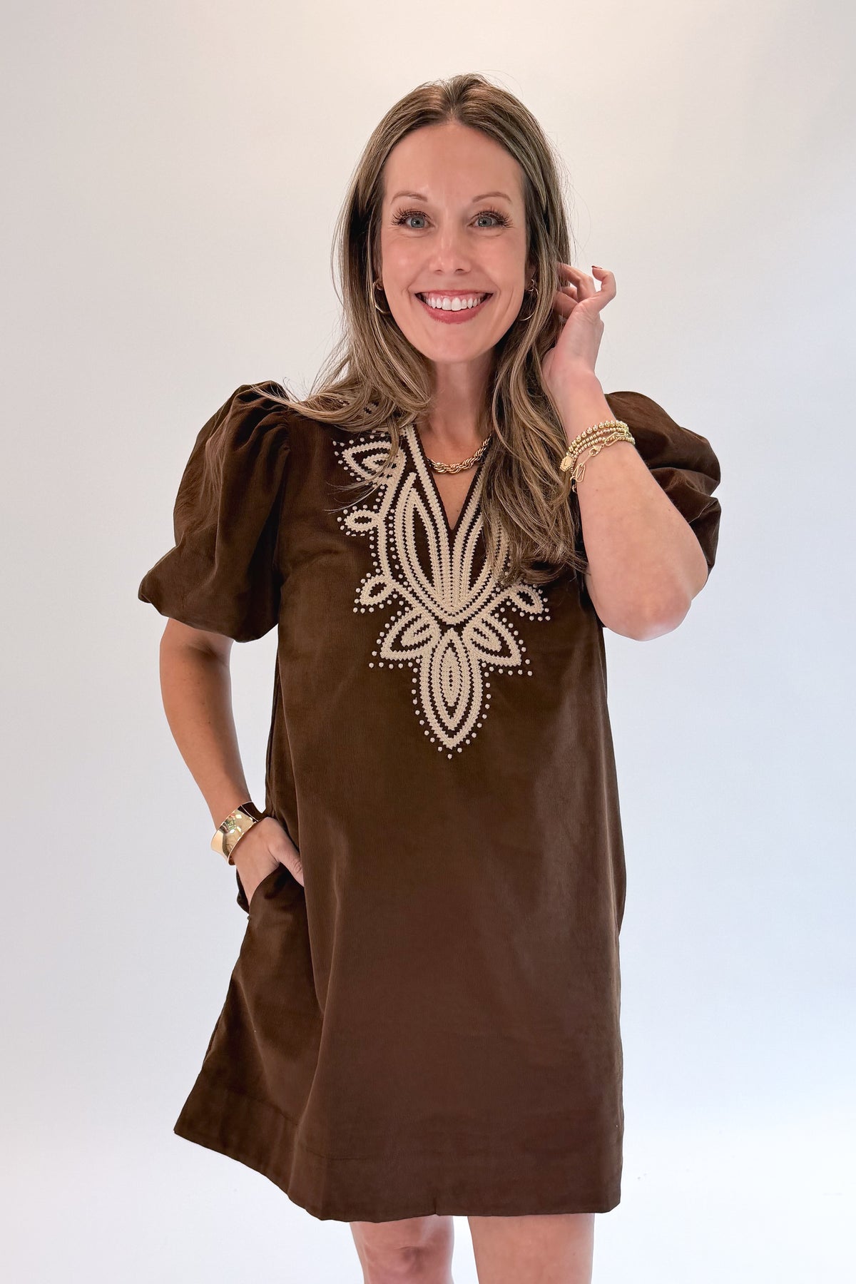 Front view of woman wearing Swagger Boutique’s Brown Embroidered Corduroy Dress with heels against white studio background.