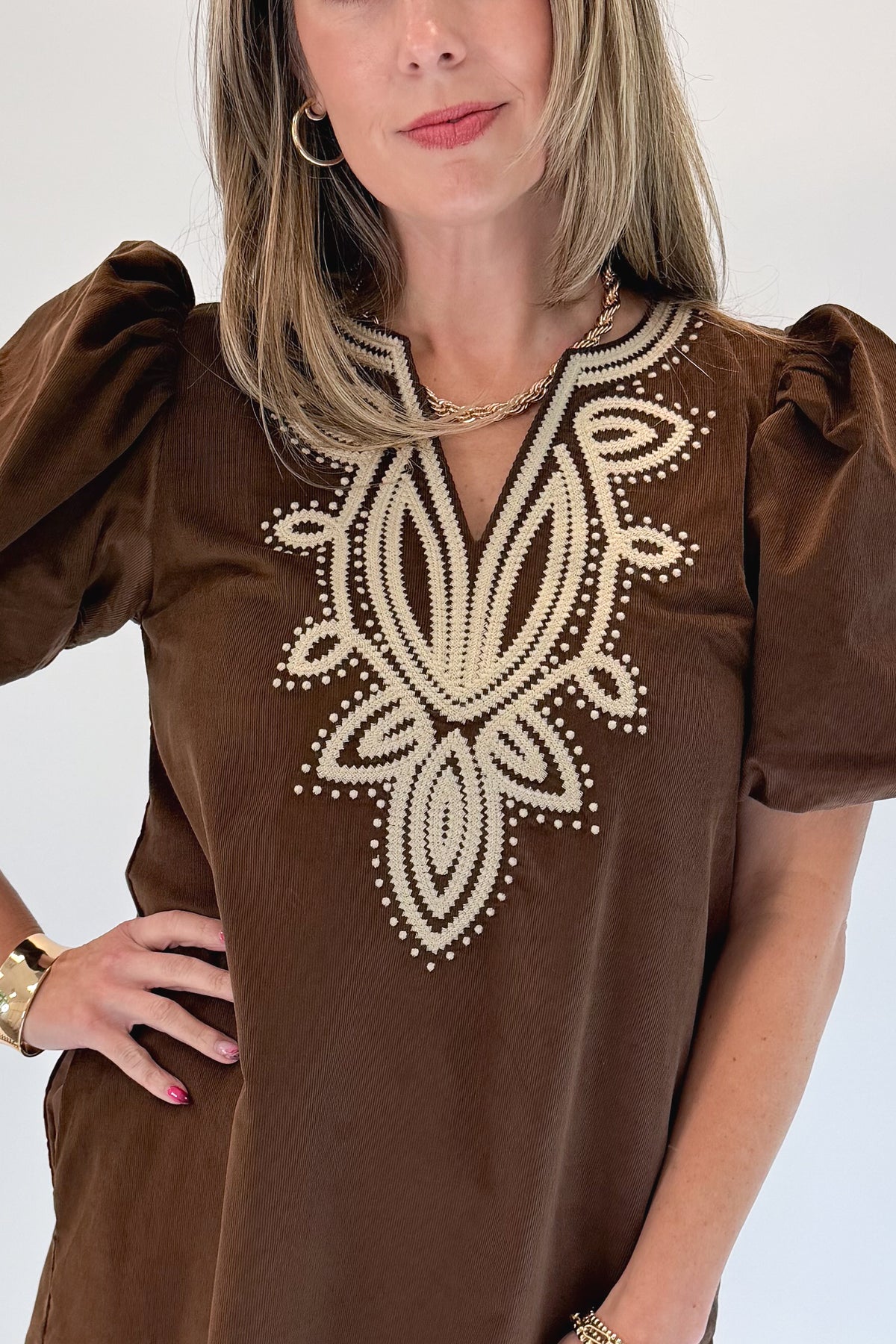 Front detail view of woman wearing Swagger Boutique’s Brown Embroidered Corduroy Dress with heels against white studio background.