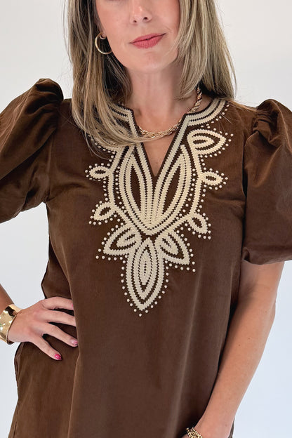 Front detail view of woman wearing Swagger Boutique’s Brown Embroidered Corduroy Dress with heels against white studio background.
