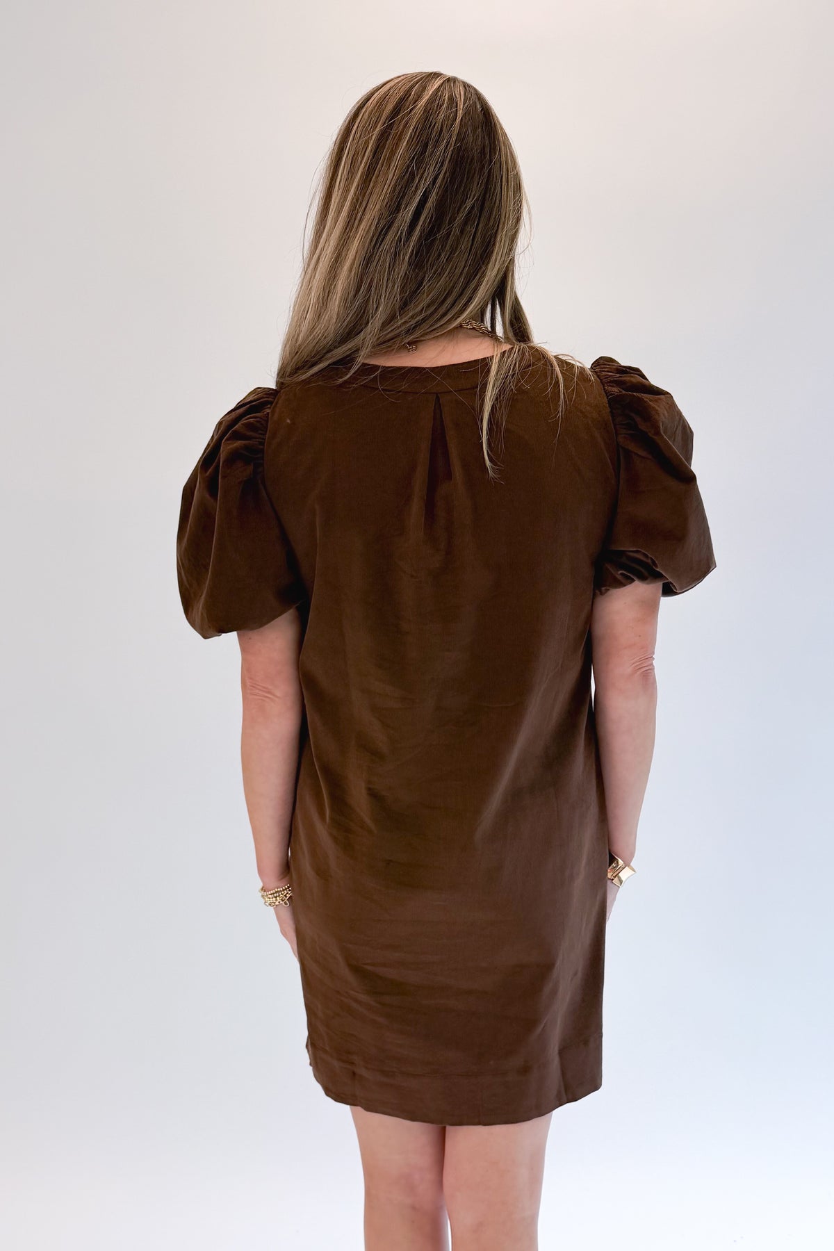 Back view of woman wearing Swagger Boutique’s Brown Embroidered Corduroy Dress with heels against white studio background.