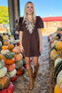 Front view of woman wearing Swagger Boutique’s Brown Embroidered Corduroy Dress with boots walking at a pumpkin patch.