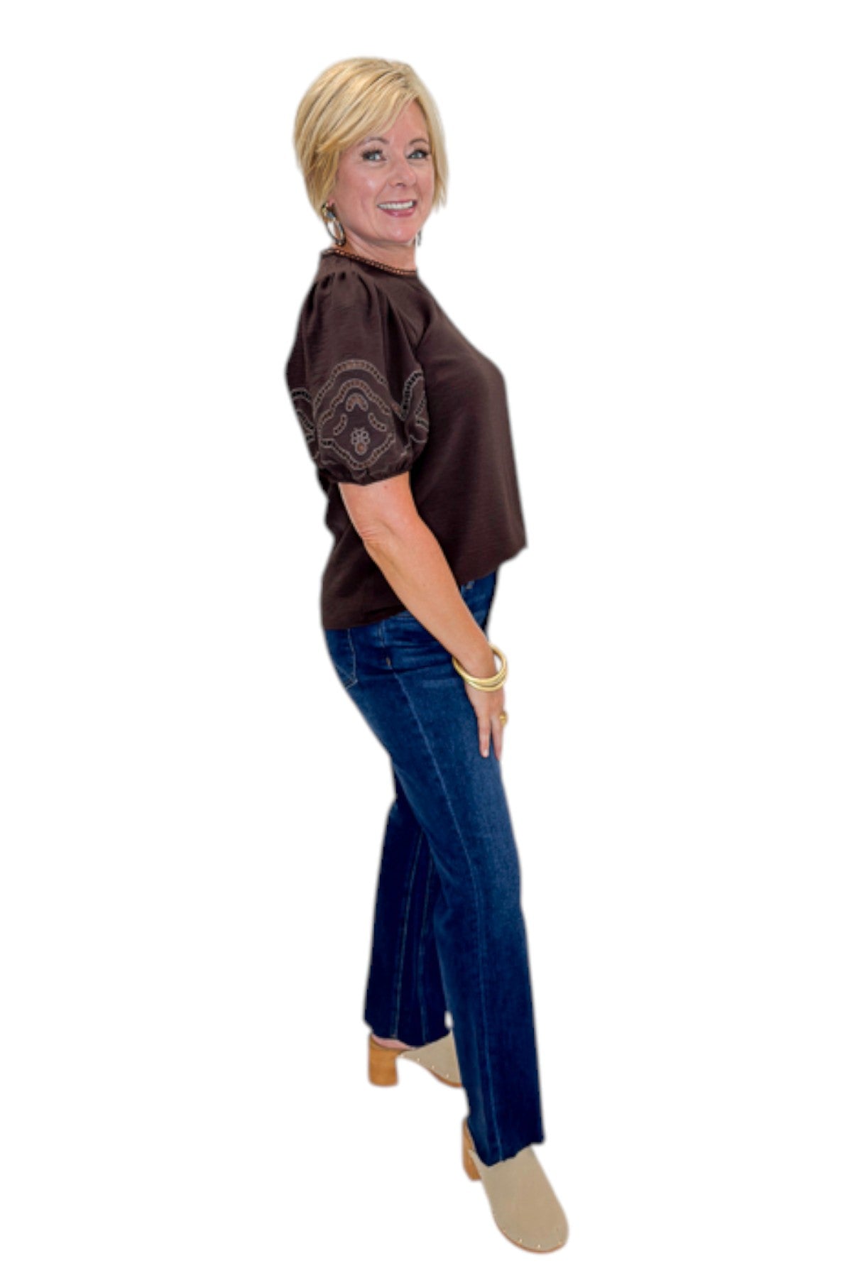 Side view of woman wearing Swagger Boutique’s Brown Embroidered Short Sleeve Top with jeans against white studio background.