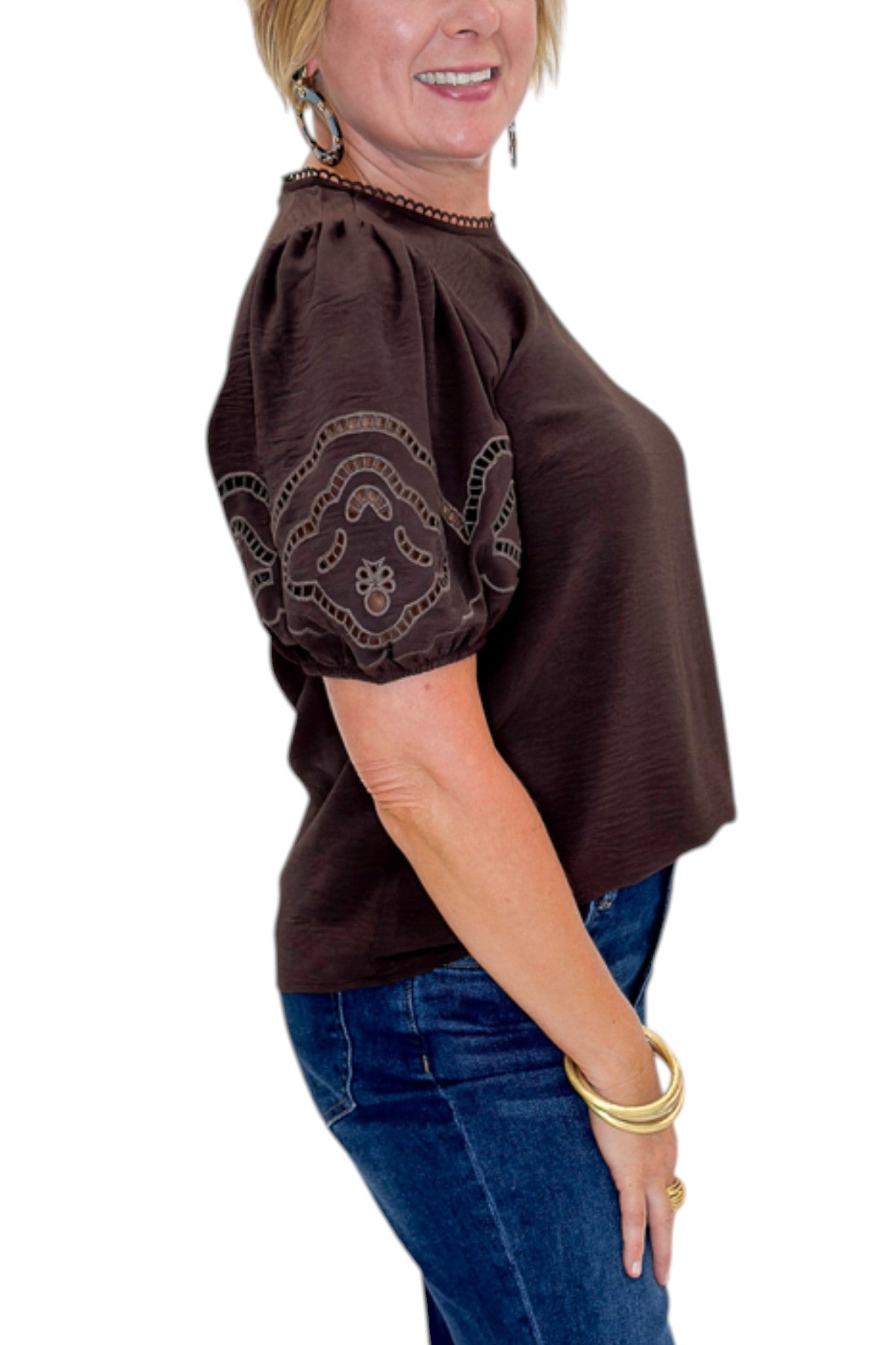 Side detail view of woman wearing Swagger Boutique’s Brown Embroidered Short Sleeve Top with jeans against white studio background.